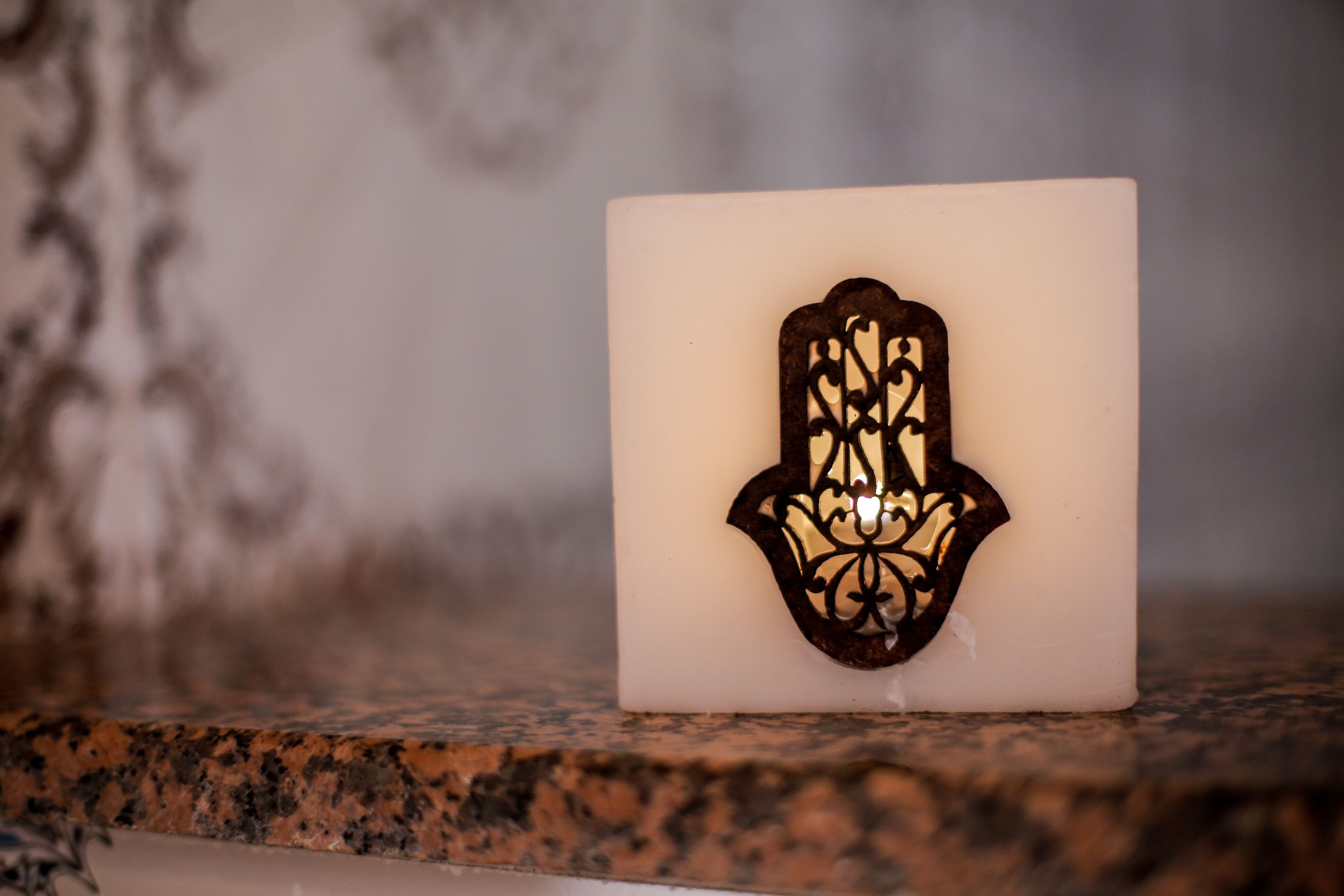 A white candle with a black Hamsa symbol on a granite countertop.