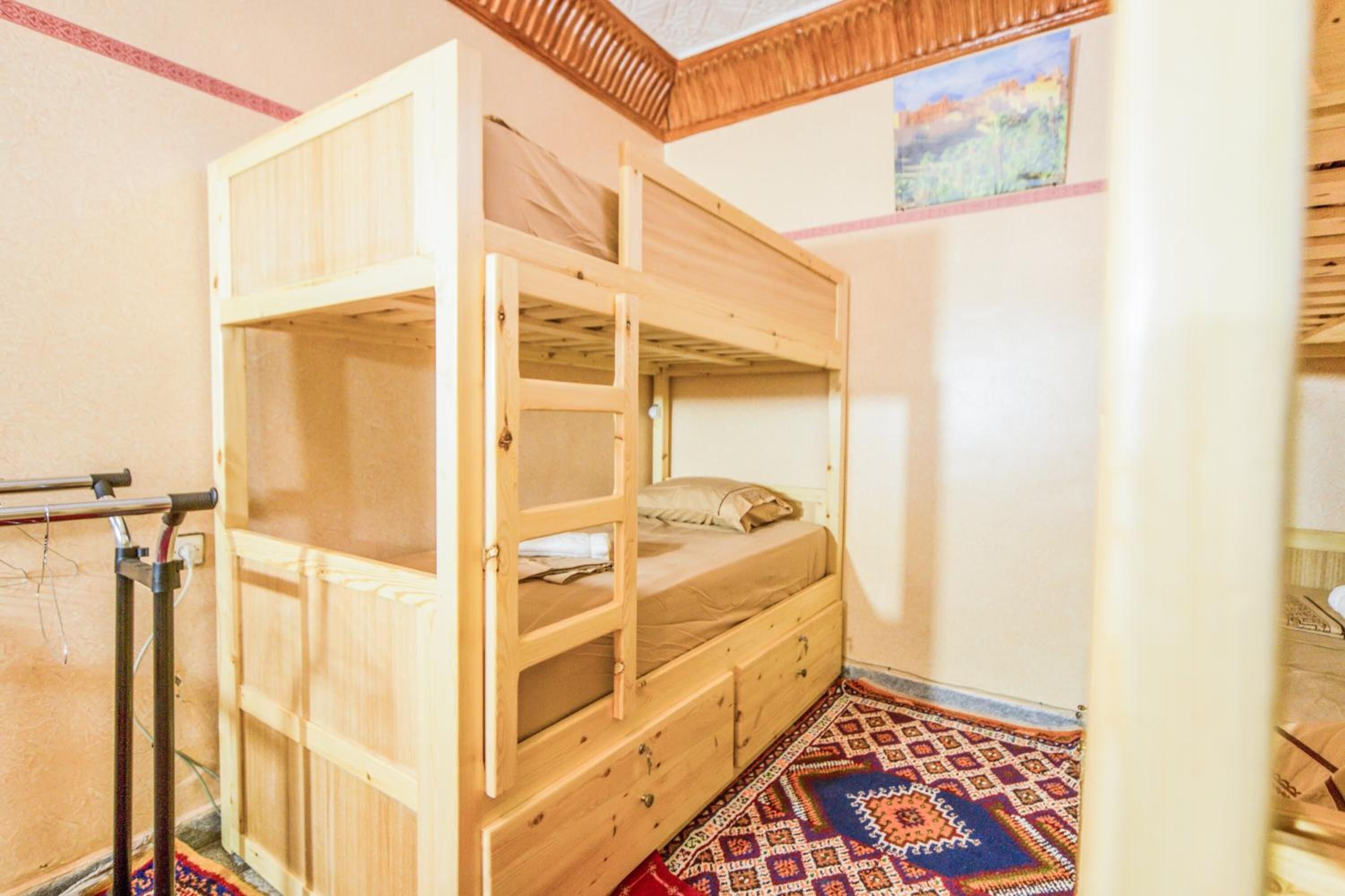 Una cama litera con estructura de madera, una mesita de noche pequeña y una alfombra estampada en el suelo.
