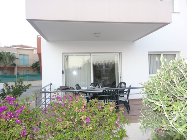 A balcony with a table and chairs, a glass door, and a view of neighboring buildings.