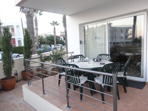 An outdoor dining area with a table and chairs, surrounded by potted plants and a railing.
