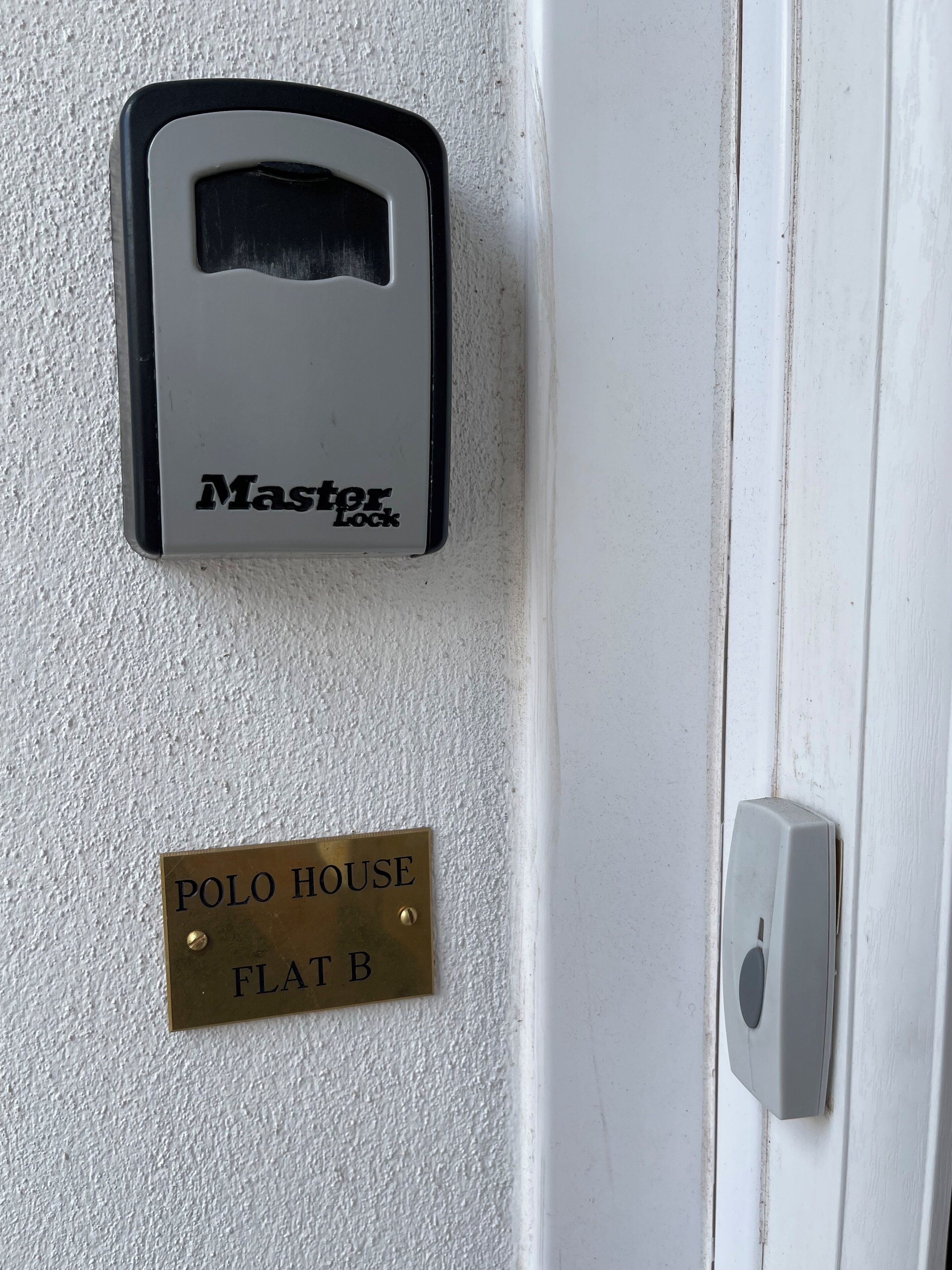 Una puerta con un dispositivo Master Lock y una placa de latón que dice "POLO HOUSE FLAT B".