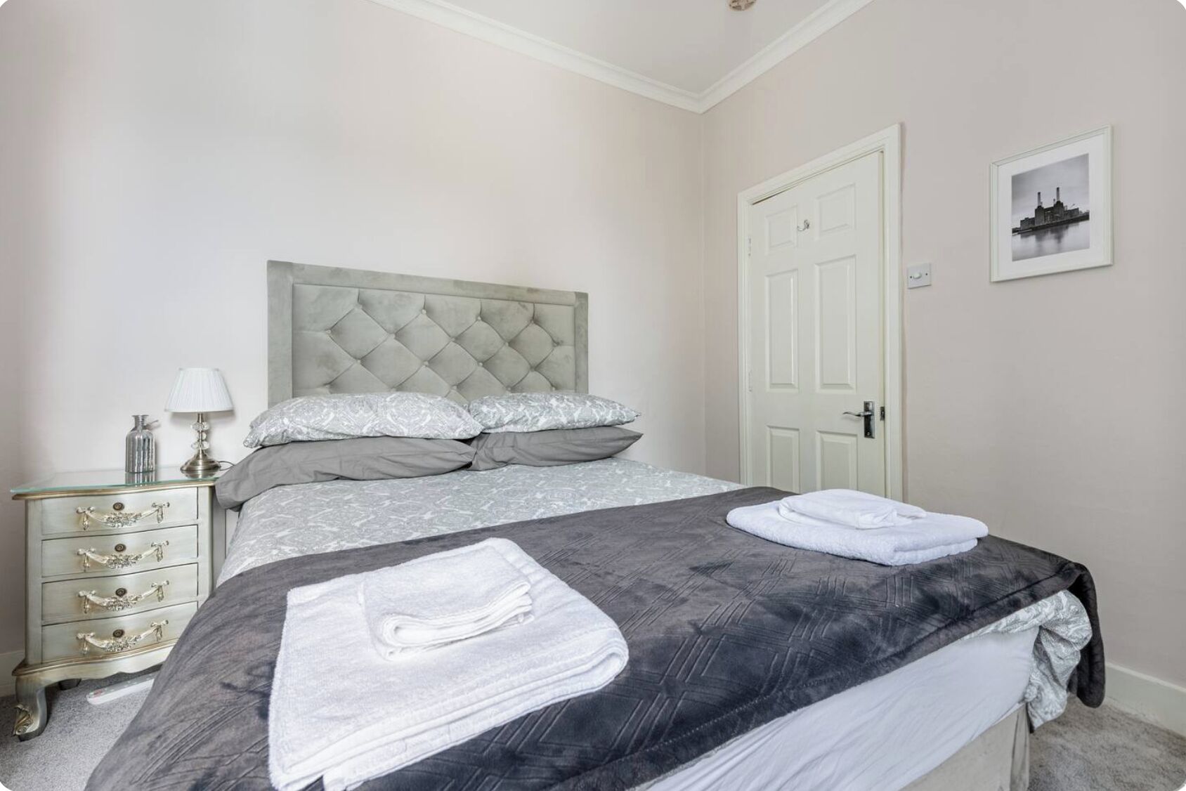 A neatly made bed with a grey and white patterned bedspread, a grey headboard, and a white door in the background.