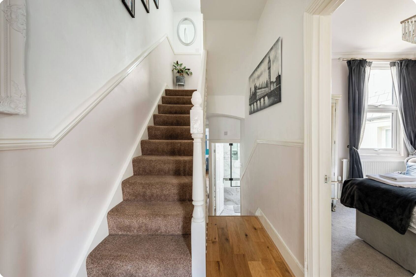 A staircase with carpeted steps leading to a room with a bed and a window with curtains.
