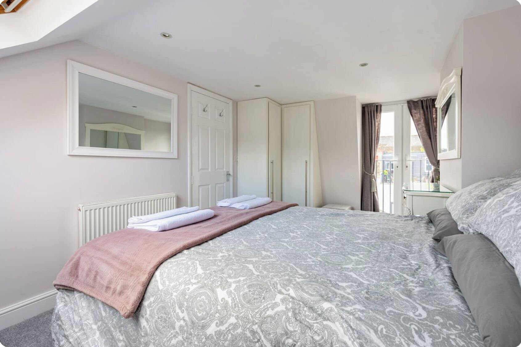 Un dormitorio con una cama grande, un armario, un espejo y una ventana con cortinas.