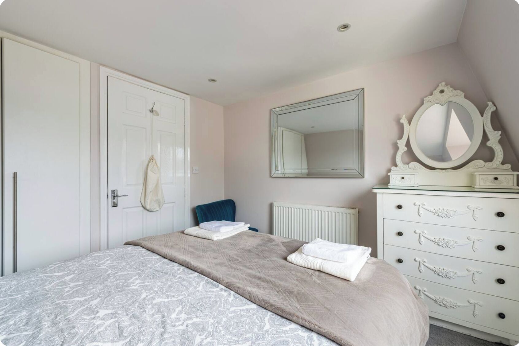 Een slaapkamer met een bed, een dressoir, een spiegel en een deur.