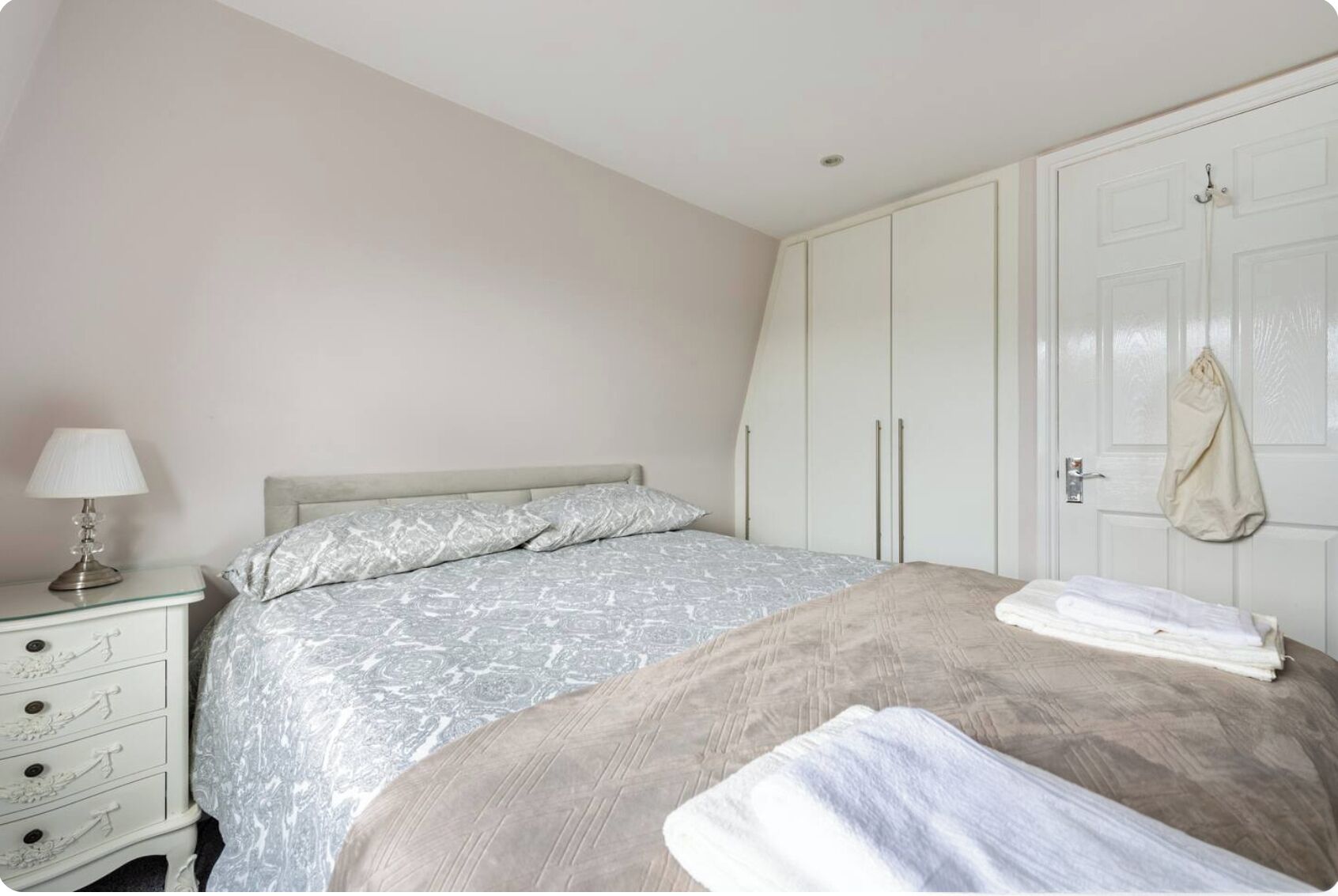 A bedroom with a bed, a nightstand, a wardrobe, and a door with a coat hanging on it.