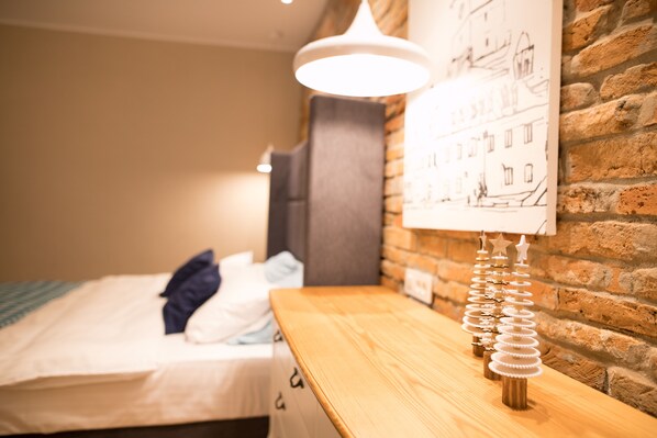 A neatly made bed with a blue pillow, a wooden nightstand with a decorative item, and a brick wall with a hanging light fixture.