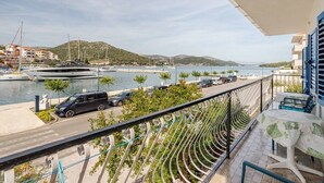 Un balcón con vistas a un puerto deportivo, una calle con coches aparcados y una montaña en la distancia.