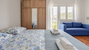 Un dormitorio con cama, sofá azul, armario de madera y ventana con cortinas.