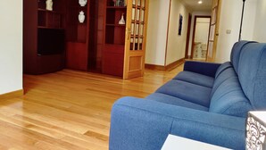 Un salon avec un canapé bleu, un plancher en bois et une bibliothèque agrémentée d’objets décoratifs.