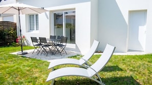 Une terrasse avec une table et des chaises, un fauteuil de relaxation et un parasol blanc.