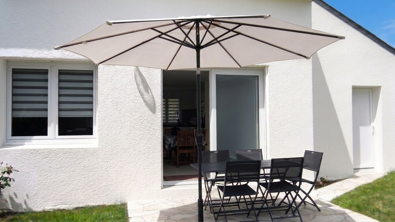An outdoor patio with a table and chairs, a large umbrella, and a white building with a door and windows.