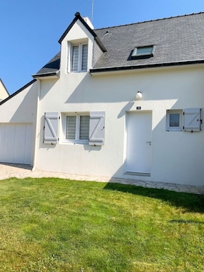 Un bâtiment blanc avec une porte de garage, une petite fenêtre et une porte sur laquelle est fixée une plaque d’immatriculation.