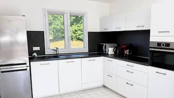 Een moderne keuken met witte kasten, een roestvrijstalen koelkast, een dubbele spoelbak en een raam met uitzicht op groen.