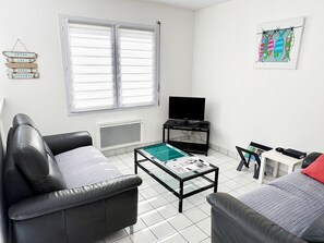 A living room with a black leather sofa, a glass coffee table, a flat-screen TV, and a small table with a chair.
