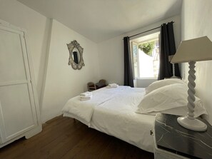 A bedroom with a bed, a nightstand, a lamp, a mirror, and a window with curtains.