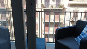 A balcony with wicker furniture and a view of a building with balconies and shutters.
