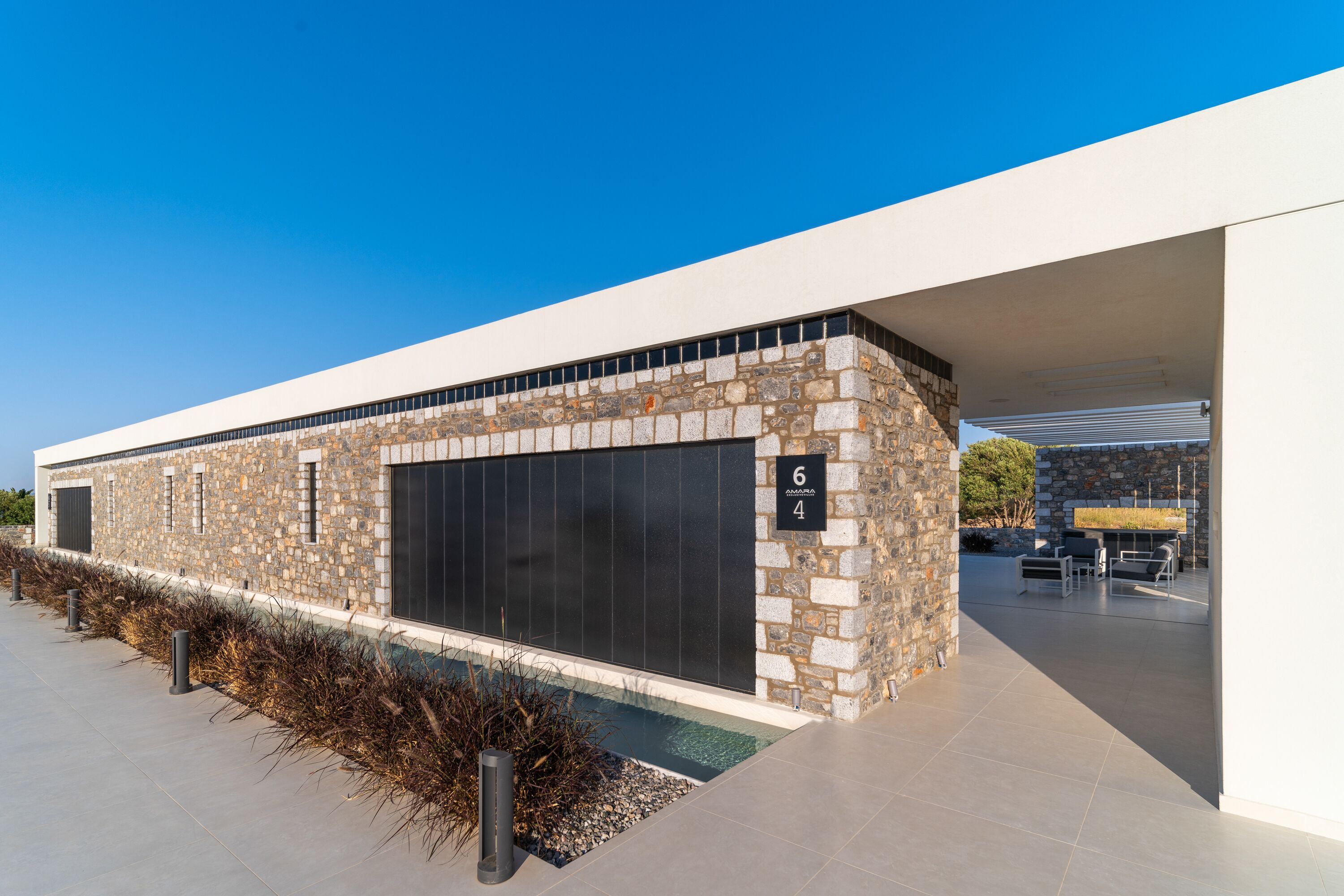 Un edifici modern amb façana de pedra, grans finestres i una zona d'estar a l'aire lliure coberta.