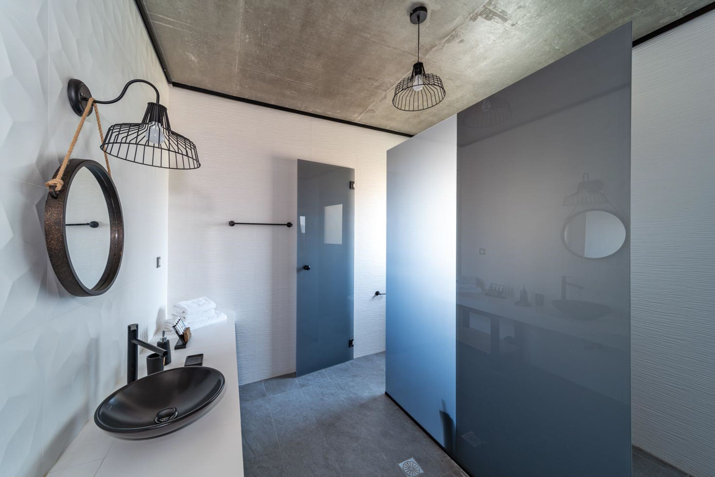 A modern bathroom with a round mirror, black sink, and two pendant lights.