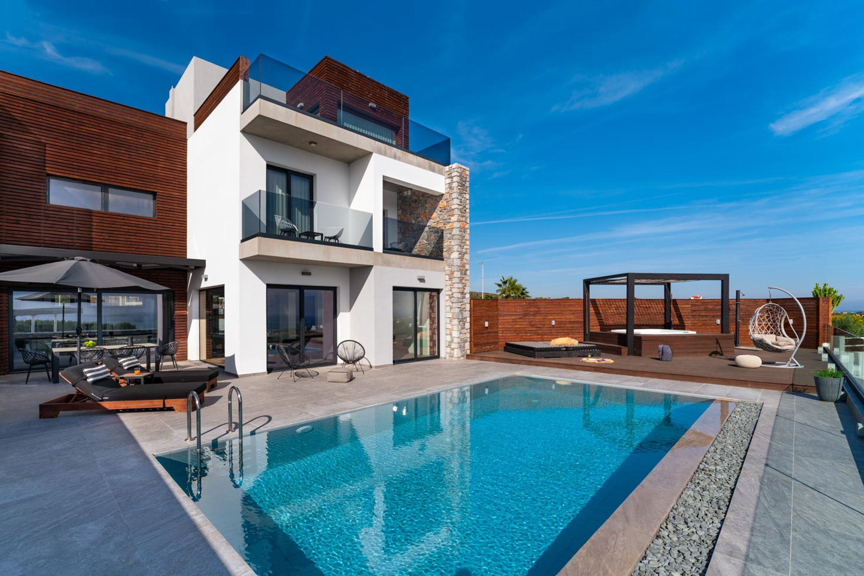A modern two-story house with a swimming pool, outdoor seating, and a view of the ocean.