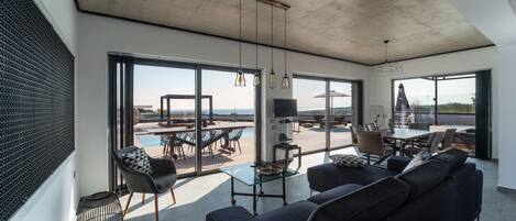 A spacious living area with a large sofa, a glass coffee table, and a pool view.