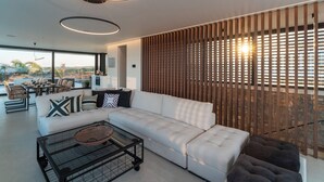 A modern living room with a sectional sofa, a glass coffee table, and a dining area with chairs and a table. - Amara Luxury villas (Rhodes)