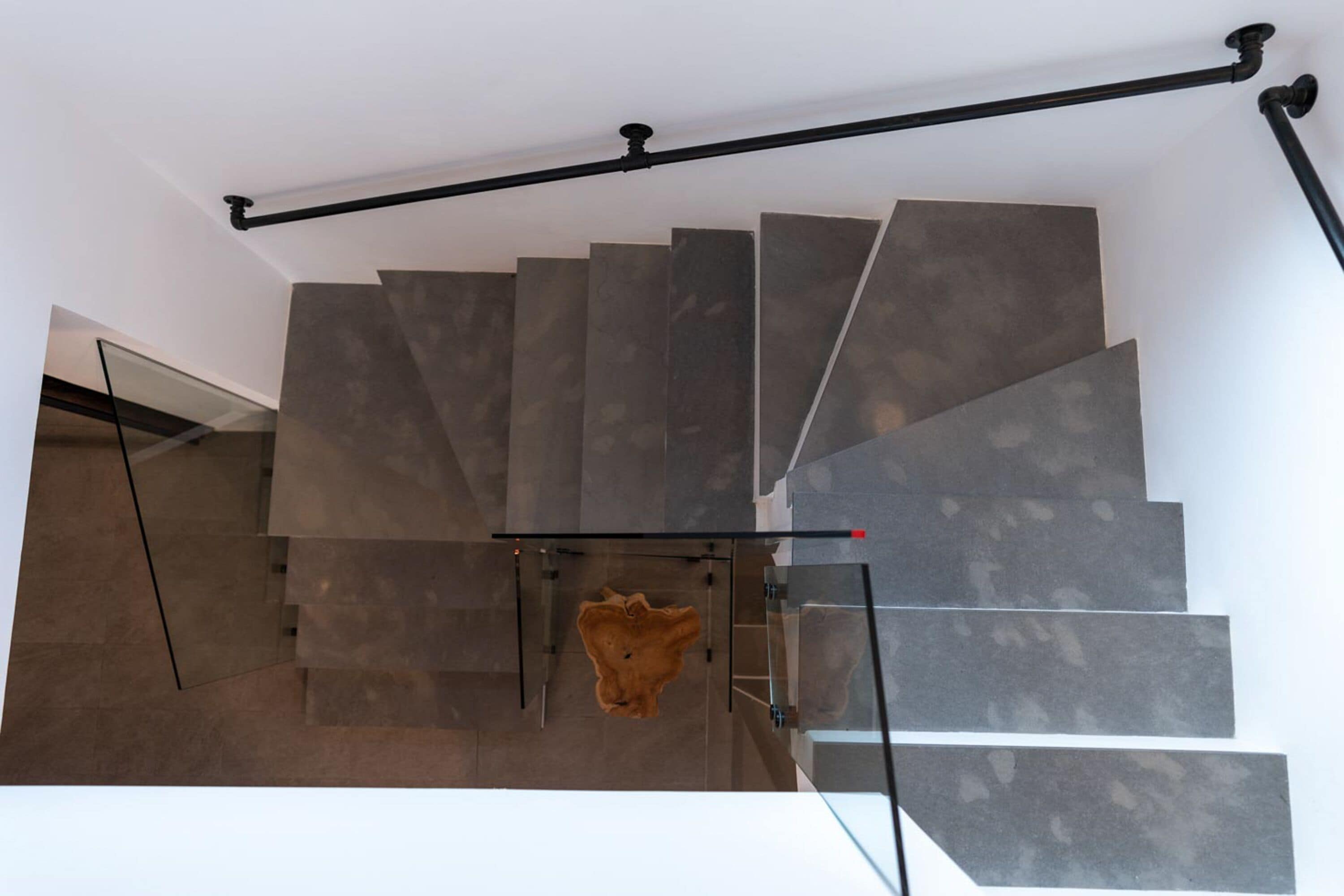 Een moderne trap met glazen leuning en een uniek houten sculptuur aan de voet.