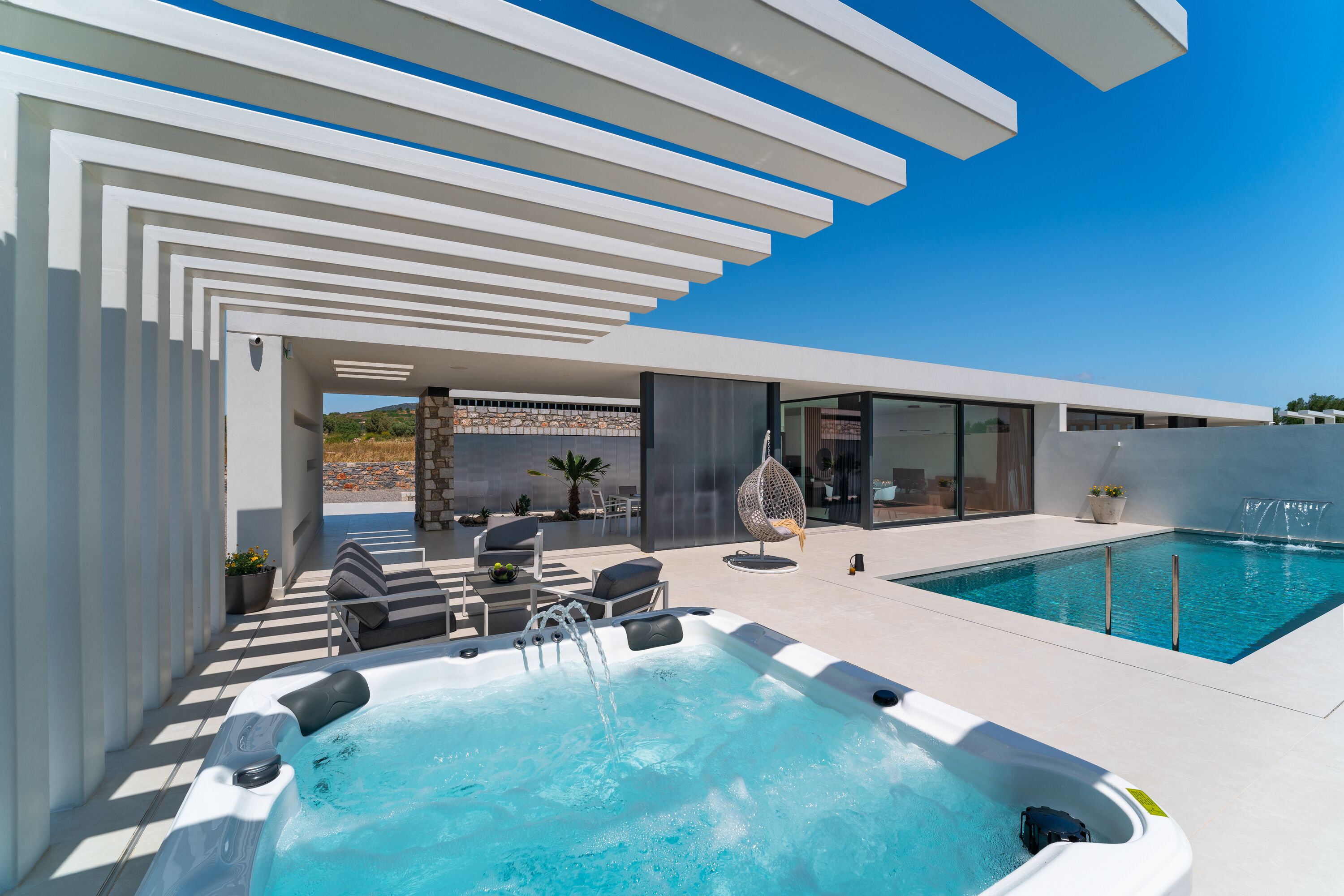 A modern outdoor pool area with a hot tub, lounge chairs, and a clear blue sky.