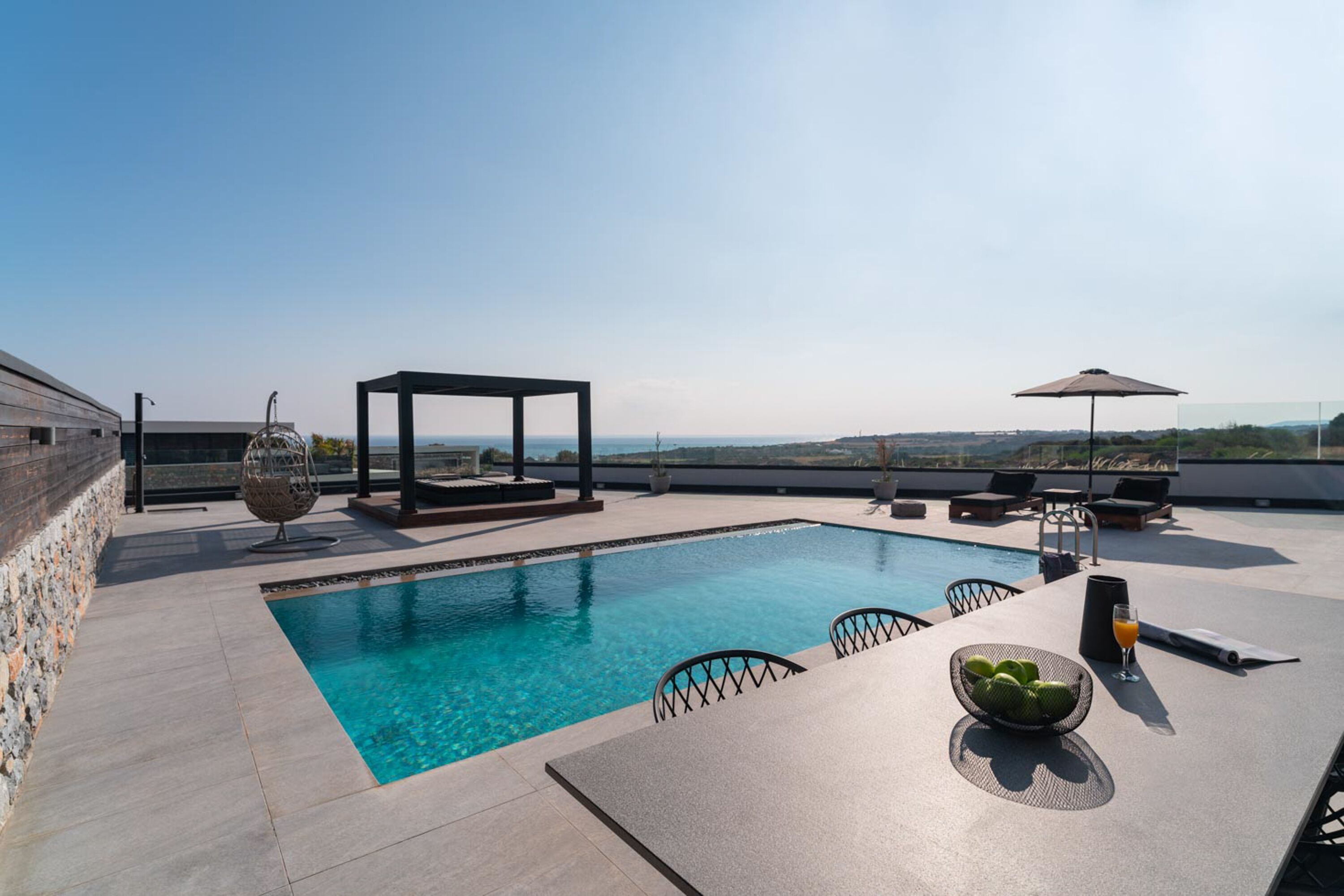 Uma área de piscina no terraço com vista ampla do horizonte, uma pérgula e espreguiçadeiras.