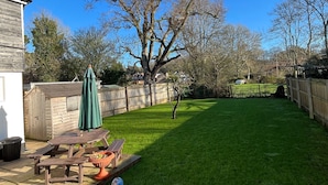 Un patio trasero con terraza de madera, mesa de picnic y sombrilla verde.