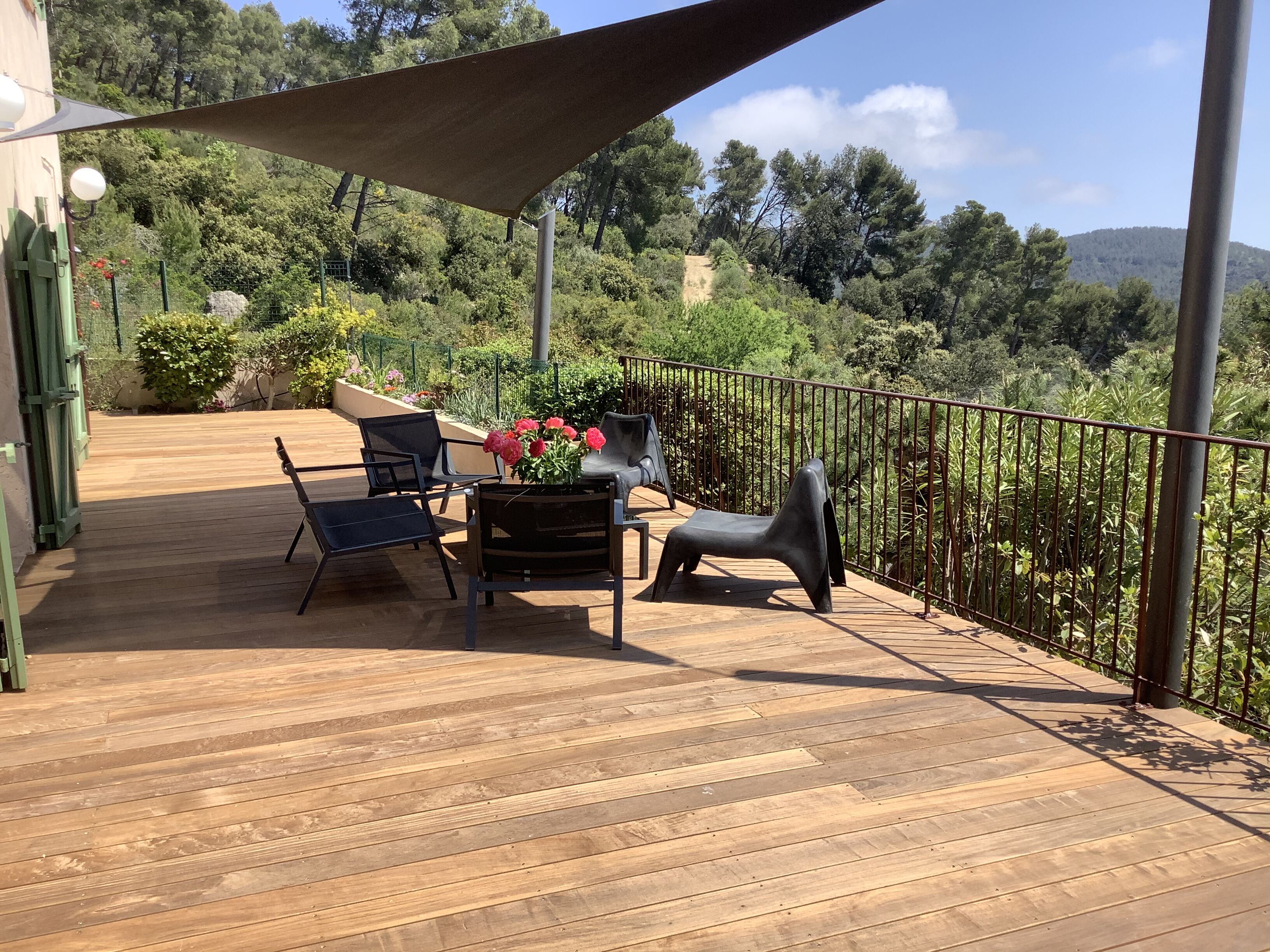 Um deck de madeira com móveis de exterior e vista para uma encosta arborizada.