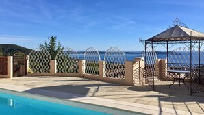 A pool area with a clear view of the sea, a gazebo, and a fenced garden.