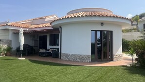 Een huis met een gebogen dak, een terras met buitenmeubilair en een stenen muur.