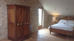 Une chambre avec une armoire en bois, un lit recouvert de draps blancs, un mur en pierre et un plafond en pente.