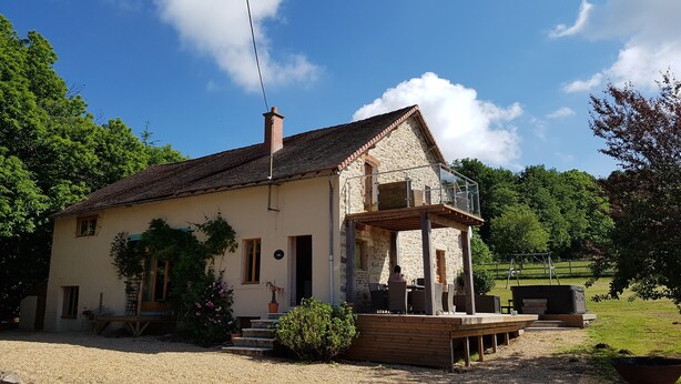 Une maison en pierre avec un balcon, une allée en gravier et un jardin agrémenté de plantes en pot.