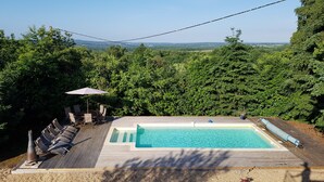 Une piscine rectangulaire avec une terrasse en bois et des chaises longues.