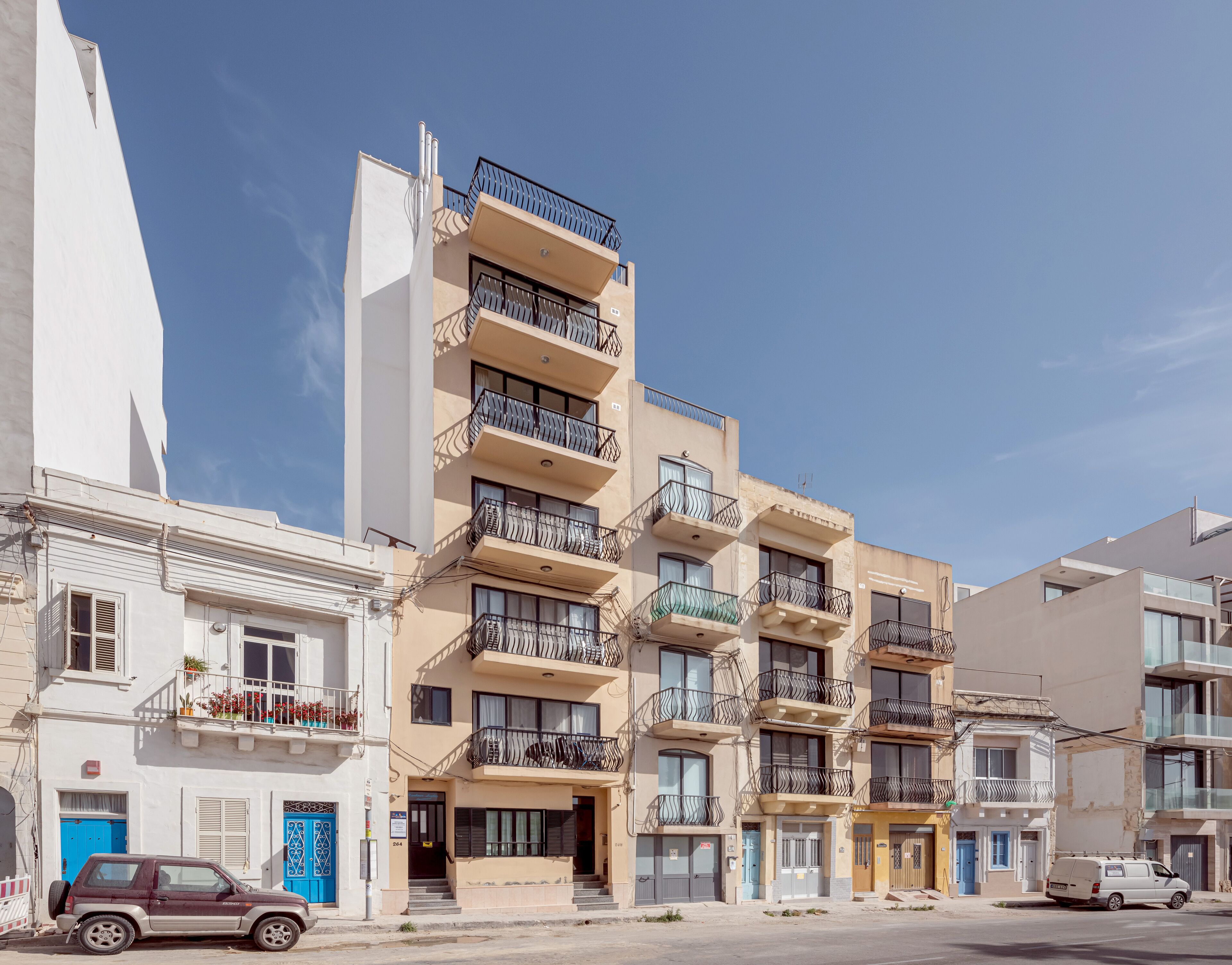 Un edificio residencial de varios pisos con balcones, una puerta azul y un coche estacionado.