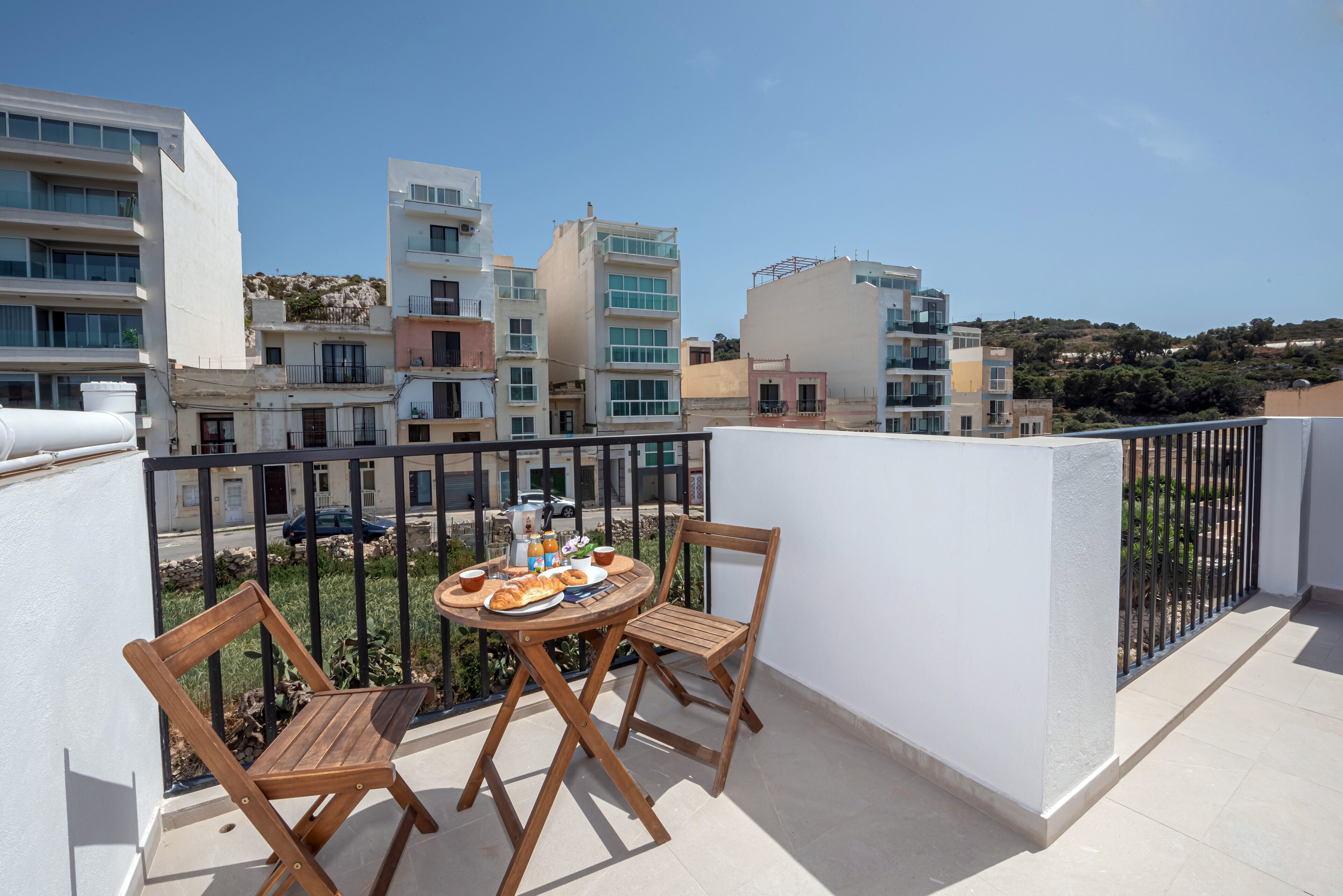Ein Balkon mit einem runden Tisch und zwei Holzstühlen mit Blick auf ein Wohngebiet mit modernen Gebäuden.