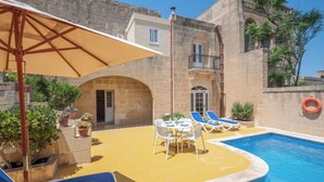 Un área de piscina con sillas de descanso, una mesa y plantas en macetas.