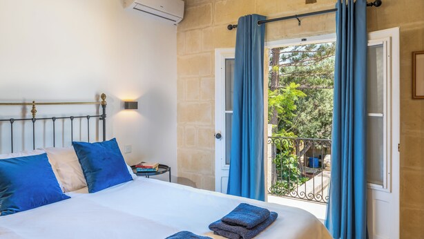 Un dormitorio con cama, cortinas azules, un balcón y vistas al verdor.