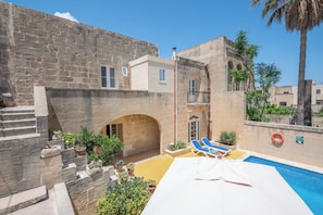 A courtyard with a swimming pool, stone walls, and a palm tree.