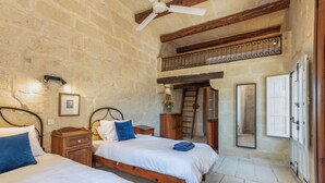 Un dormitorio con dos camas, cabeceros de madera, un ventilador de techo, una escalera de madera y una pared de piedra.