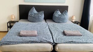 A double bed with a grey and white patterned bedspread, two matching pillows, and a pair of bedside lamps. - Pension Kellei 71 (Dresden)