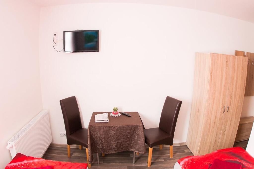 Ein kleines Zimmer mit einem Bett, einem Tisch mit zwei Stühlen, einem an der Wand montierten Fernseher und einem Kleiderschrank.
