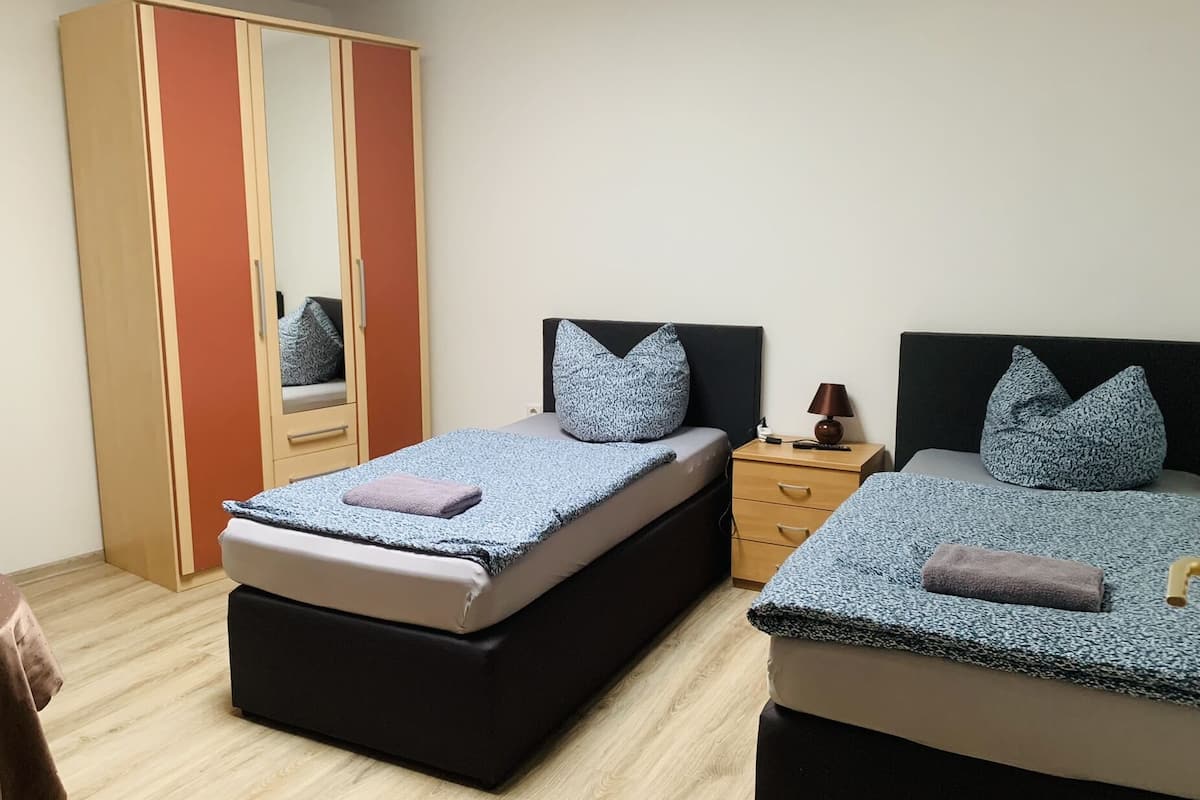 A bedroom with two beds, a wardrobe, a nightstand, and a table.