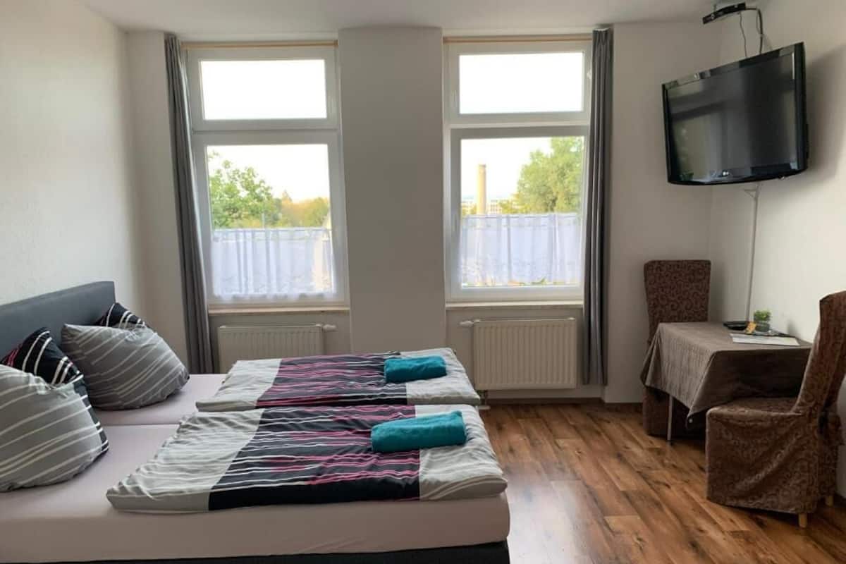 A hotel room with two beds, a TV, a small table, and a chair.