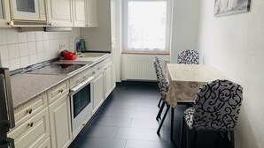 A kitchen with white cabinets, a microwave, a stove, and a dining table with patterned chairs. - Pension Kellei 71 (Dresden)