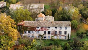 Un grand bâtiment blanc, doté d’un toit recouvert de tuiles, entouré d’arbres et de verdure.