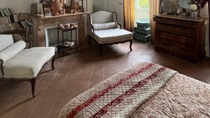 Une pièce comprenant un lit, une chaise, une petite table, une commode, un miroir et une fenêtre avec des rideaux.