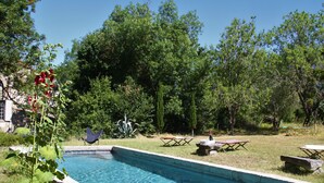 Une piscine entourée d’une pelouse, d’arbres et de mobilier d’extérieur.